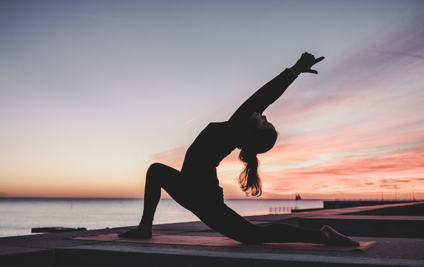 A practitioner in a low lunge silhouetted against a sunset sky